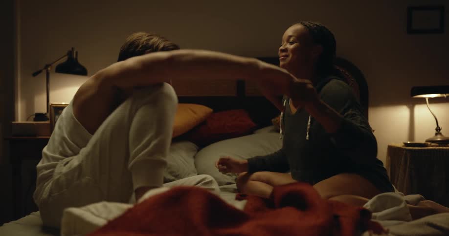 Young couple sitting in the bed hold hands and passionately kiss before lying down playfully