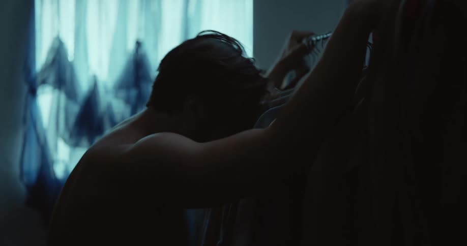 Muscular shirtless man with glasses and beard cries and holding pipe clothing rack in room