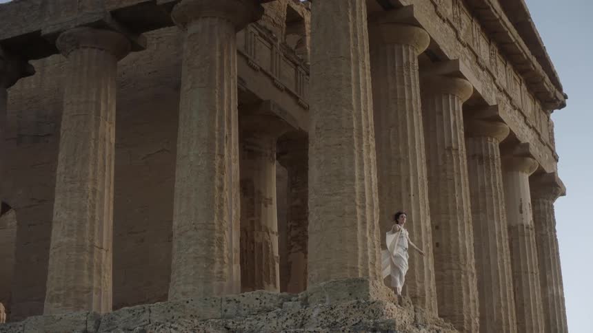 A woman wearing white robes stands outside on a windy day