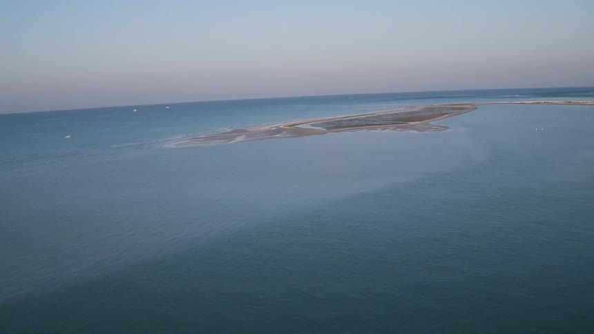 An island is surrounded by blue water as birds fly over