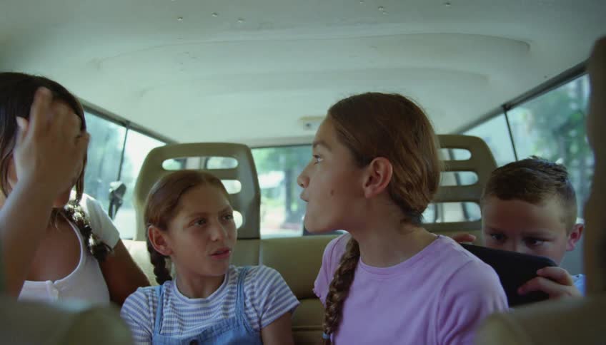Children are talking and playing around as they ride in the back of a van as it travels on a road