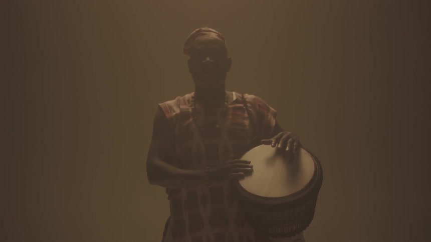 Man standing in dim room holding a bongo drum