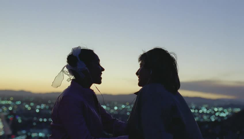 Silhouette of a young couple talking and smiling in front of a small city at evening