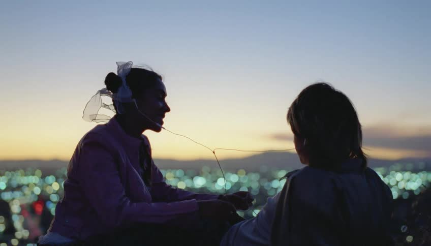 Silhouette of a young couple talking and smiling and sharing earbuds in front of a small city at evening