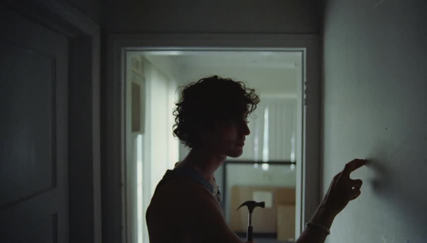 Youth holding hammer stands in hallway tapping on wall to find a stud