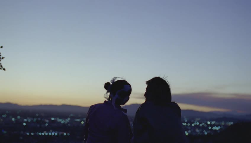 Silhouette of a young couple talking and smiling in front of a small city in the evening