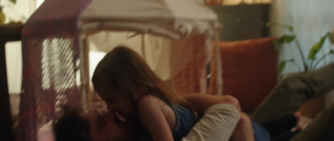 A dad sitting on the floor opens his arms wide for his daughter hugging and kissing her
