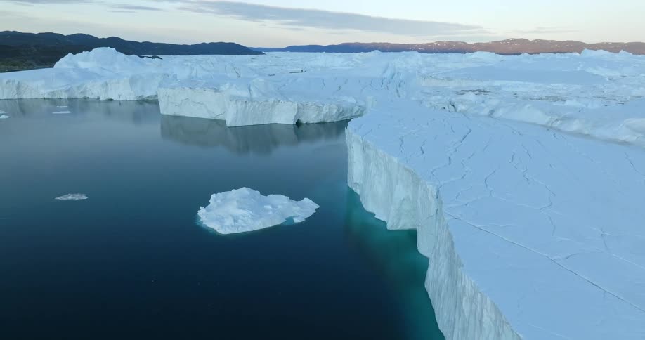Aerial view of a glacier meeting with the ocean next to the mountains at evening