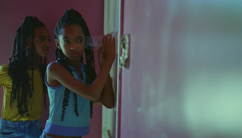 Two young girls are standing next to a door listening to what is going on outside the door