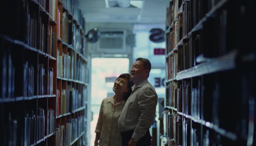 Man and woman wearing shirts stand in front of bookshelves looking at books in the library