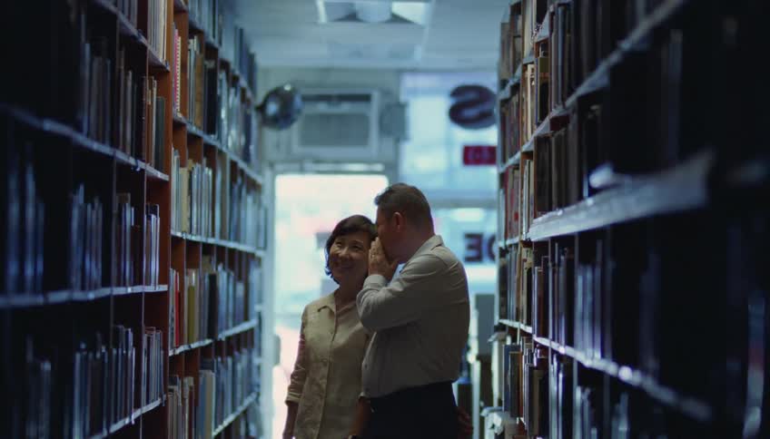 Relaxed couple whisper to each other while looking at books in a bookstore