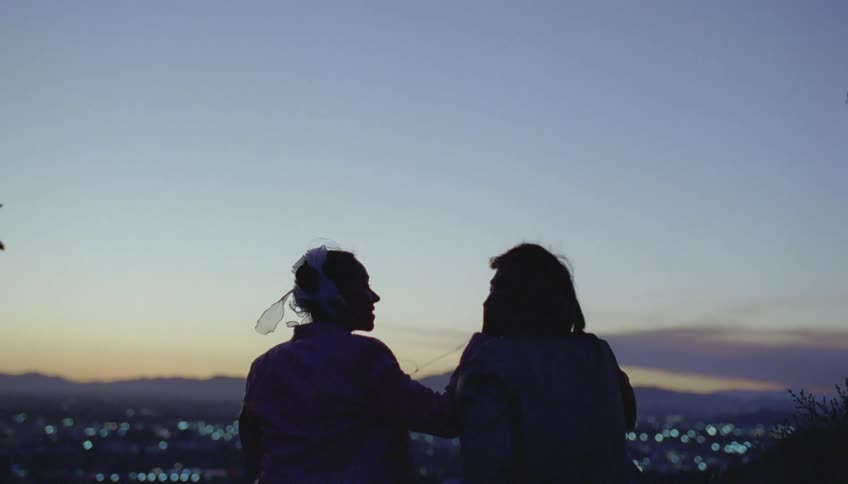 Man and woman wearing earphones are silhouetted against the sky and city view