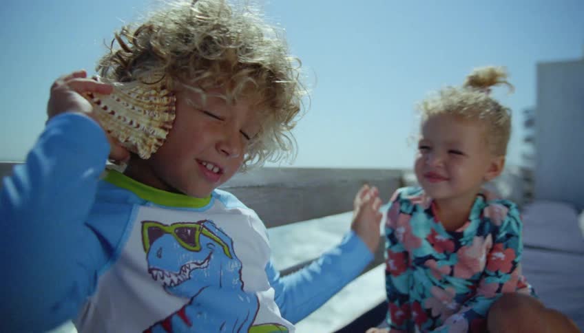Kids listen to seashell as they sit near rail overlooking ocean water