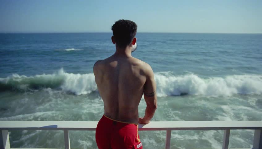Man standing at rail watching waves crash turns to make announcement over a megaphone