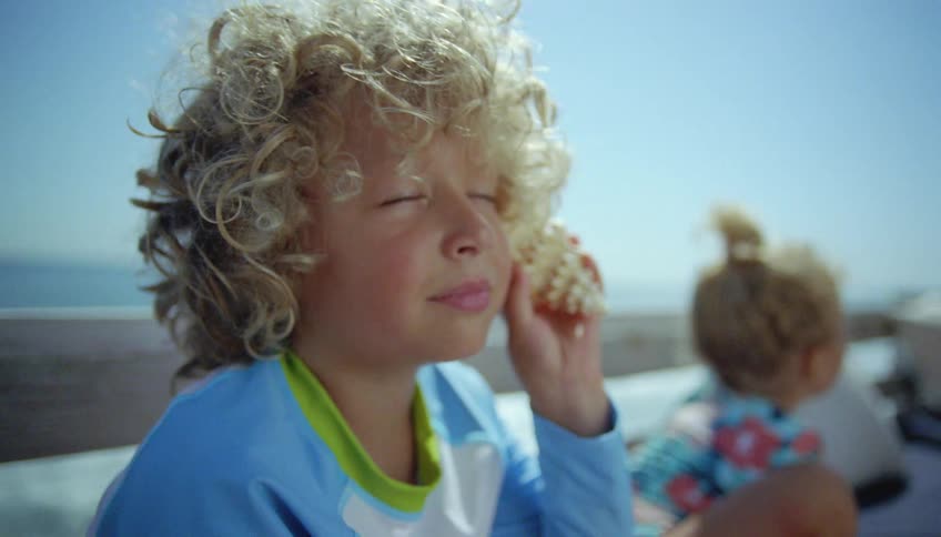 A child is listening to a sea shell on the beach