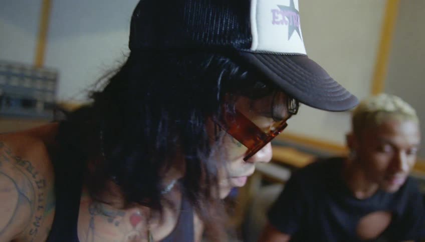 Male sound engineer with cap wavy hair sunglasses and black undershirt adjusts mixing console in cutting room recording studio