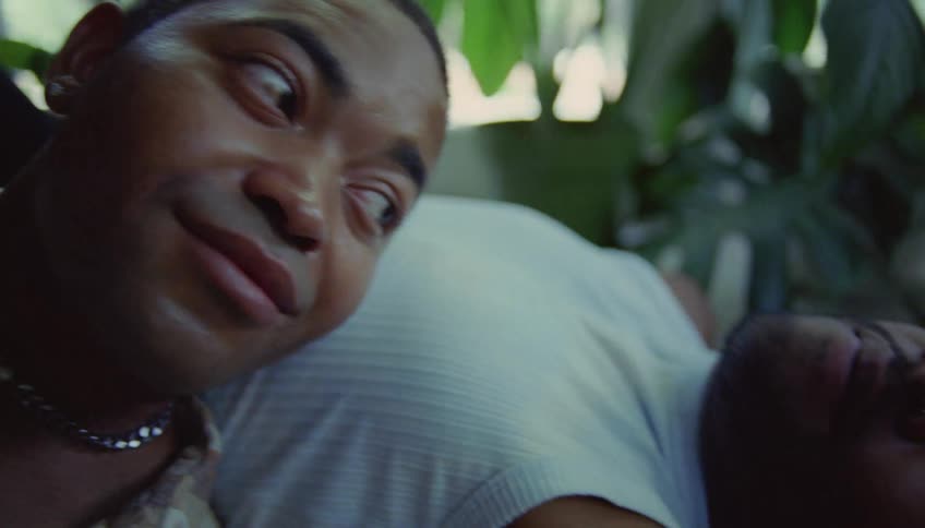 A man lies on the floor and looks at a man who smiles at him with his head resting on his chest