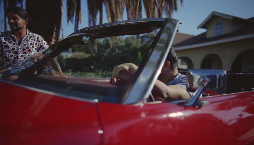 Men admire a vintage red car parked on the house driveway