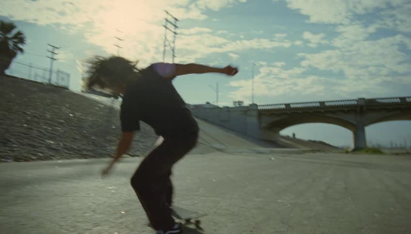 A teenage boy is riding a skateboard and he almost wipes out doing a kick flip as he rides towards an underpass
