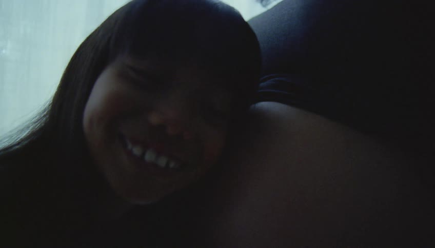 Daughter listens to pregnant mothers belly with wavy hair and white shirt smiling