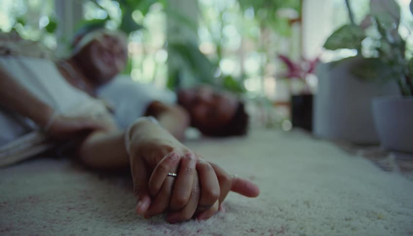 Two people are lying on the floor holding hands and wiggling their fingers