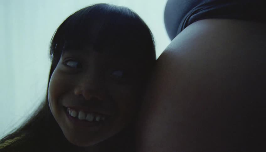 Sister to be smiles while pressing ear to mothers pregnant abdomen