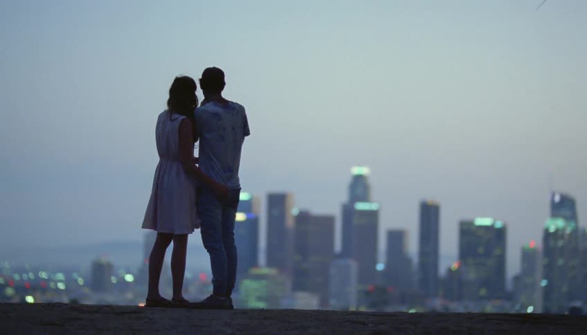 A couple stand before the city on a windy day