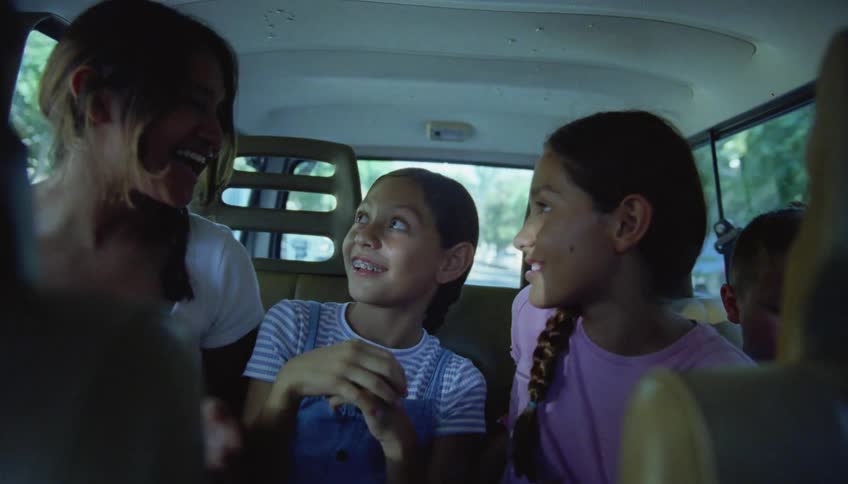 Three sisters sit in the back of a vehicle next to their brother and laugh and talk