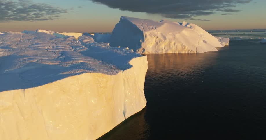 Sunlight shines on large pieces of ice floating in the water under a cloudy sky
