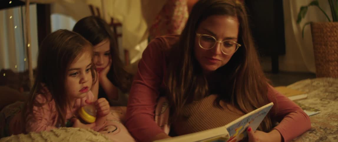Mother reclines next to daughters while reading to them from a book