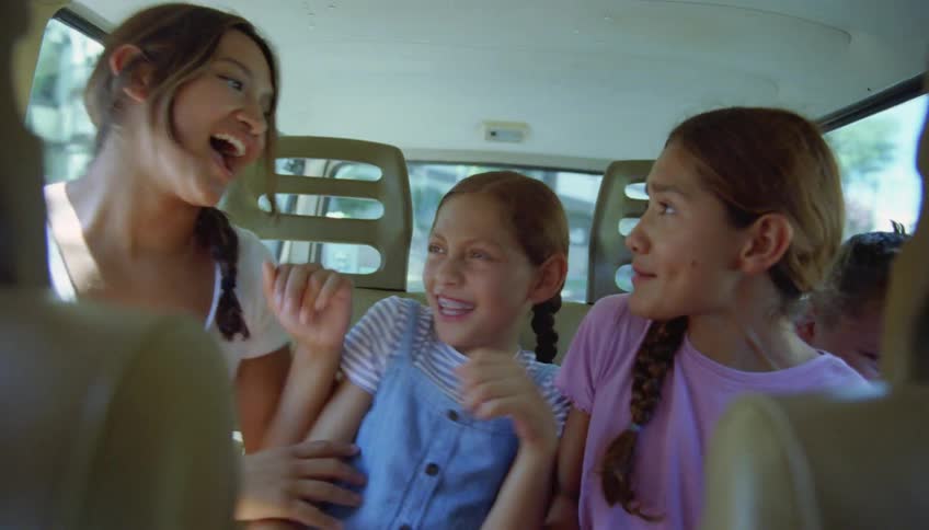 Sisters sitting on the backseat of a moving car playfully push each other while talking and laughing