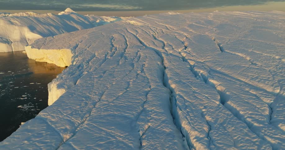 Aerial view of the cracked surface of a glacier meeting with the ocean at sunset