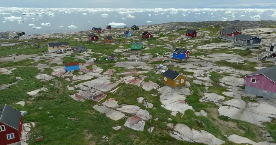 Aerial view of coastal town with cottages next to ocean with ice fragments
