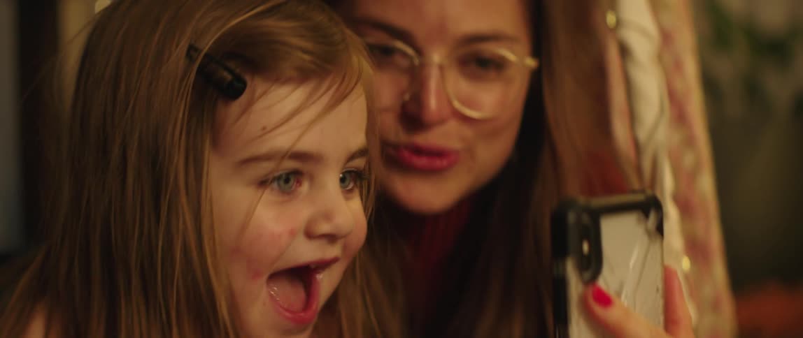 A mom holds up a phone for a video call as her little girl smiles and laughs
