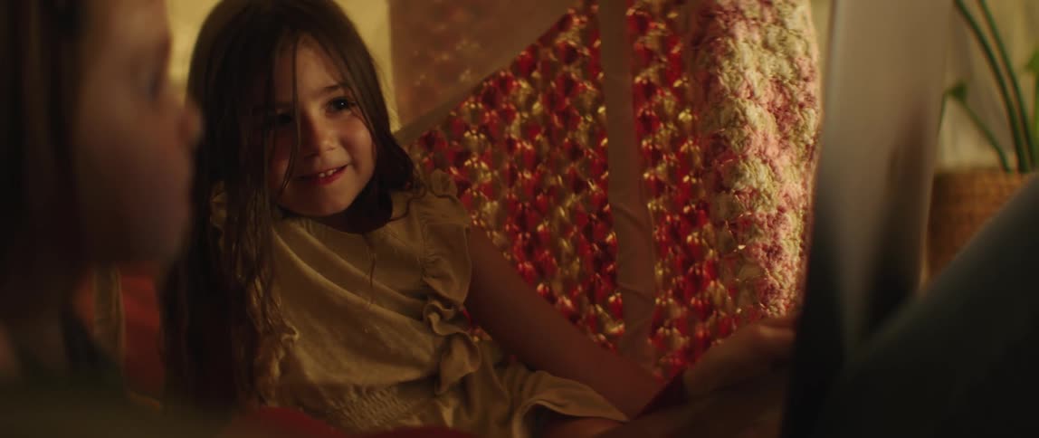 Two little girls are sitting together and smiling in a blanket fort