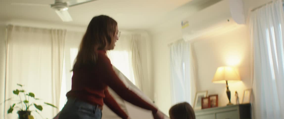 Mother with brown wavy hair red sweater and jeans plays with daughters in living room