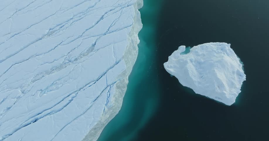 Iceberg floats on mirror like water near ice covered coast