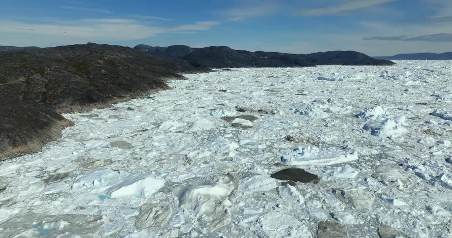 Ice and snow covered water and rock at the base of mountains under a bright blue sky