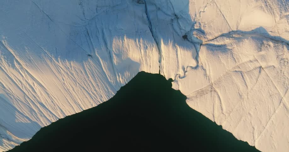 Top down aerial view of the rugged slopes of a glacier meeting with the ocean