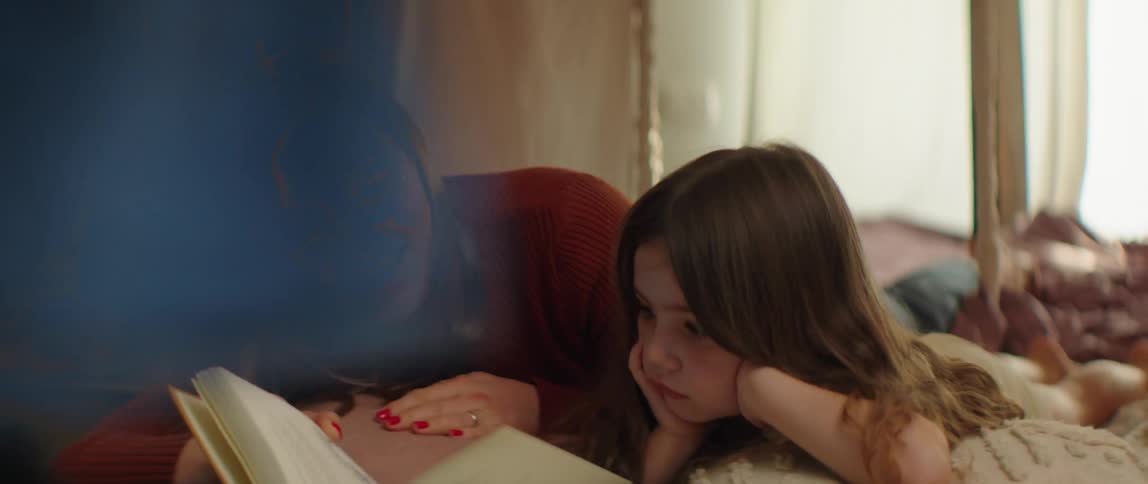 A woman is lying on the floor with her young daughter reading a book