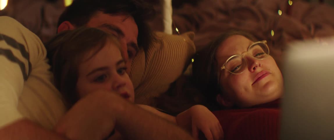 Father mother and daughter lie in bed watching laptop in bedroom