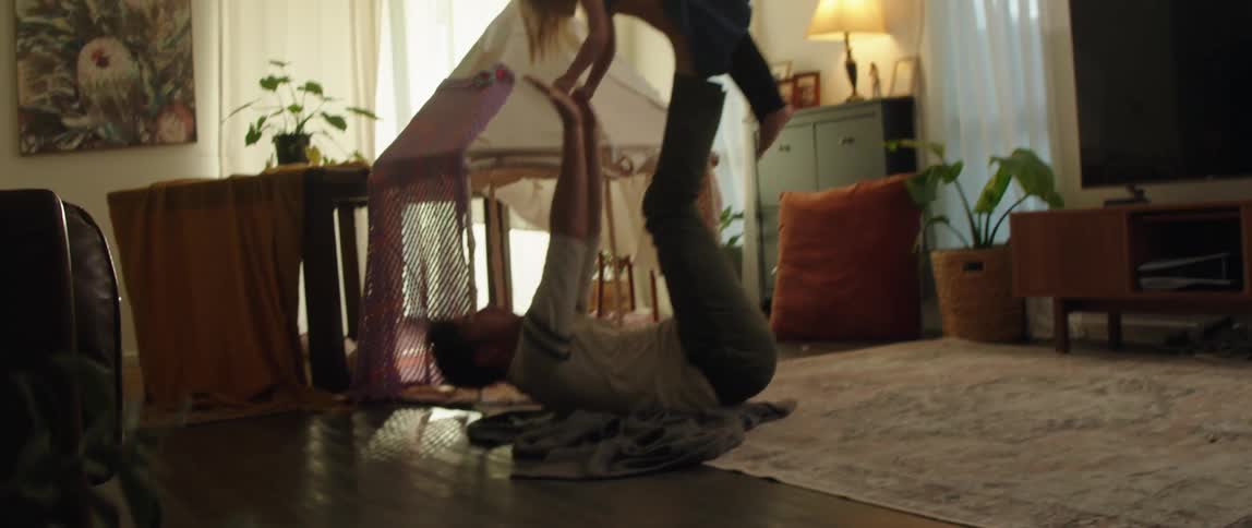 A father lying on his back holds his daughter up in the air on his feet while he holds her hands and then they laugh as he lowers her to the ground