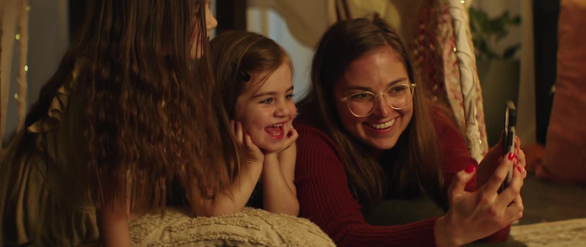 Mother laying in the floor of the living room with her daughters looking at funny videos on the smartphone