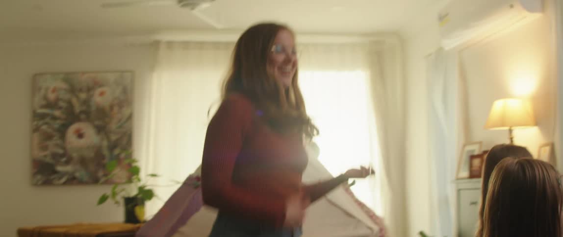 A woman plays air guitar while dancing with her daughters in their living room
