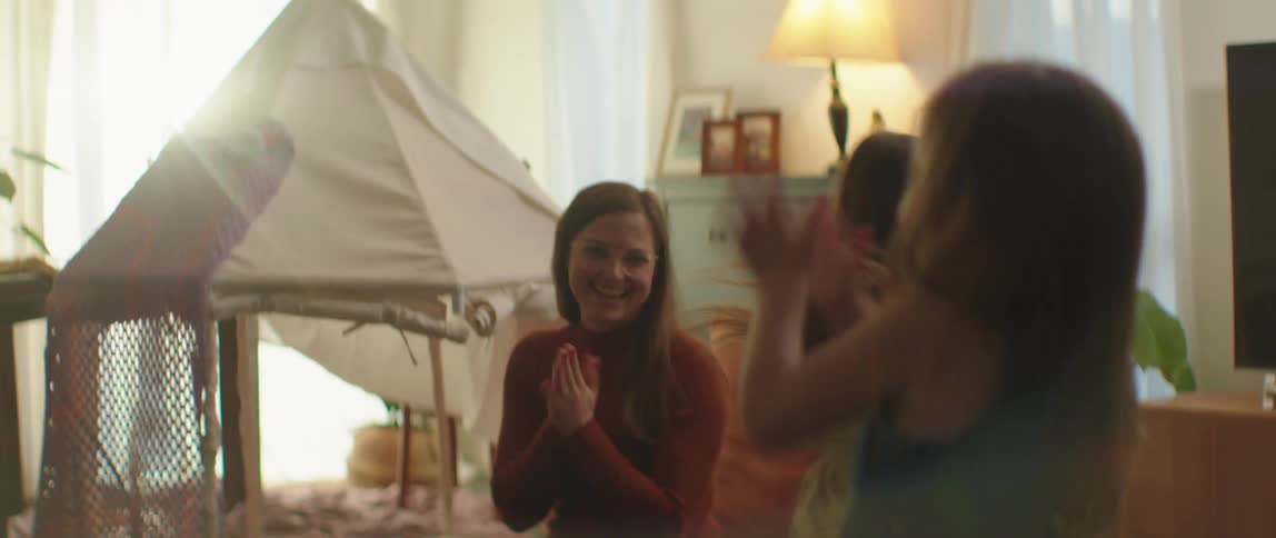 A woman claps and laughs as she watches her daughters dancing and leaping