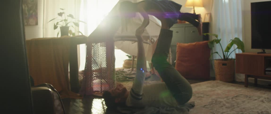A dad rolls backwards lifting his little girl up into the air on his feet