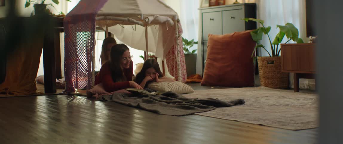 Mother lying on the floor of the living room with her daughters reading a storybook