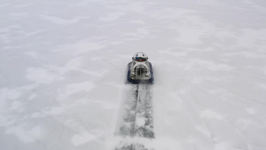 Aerial view of a hovercraft blowing snow while sliding over the frozen surface of a lake