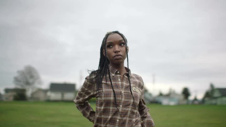 A woman standing in a grass clearing near homes looking strong and defiant