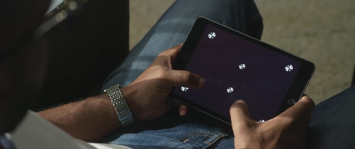 Man with jeans, glasses, and silver wristwatch sits on couch using tablet